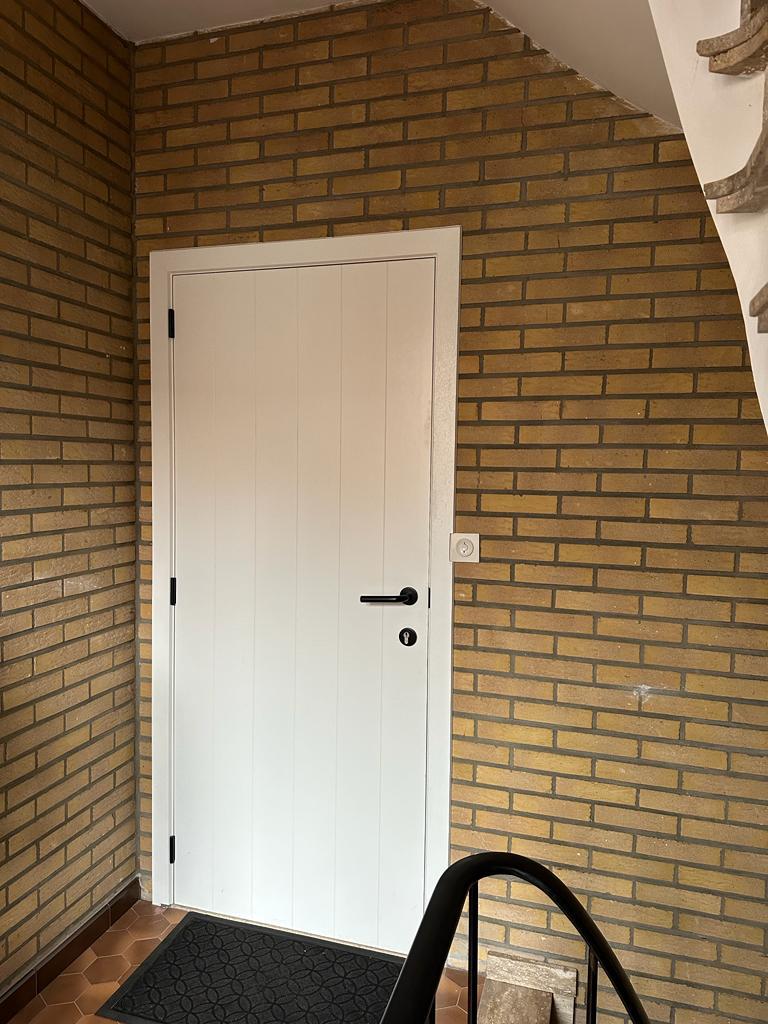 Witte deur in bakstenen muur met trapleuning